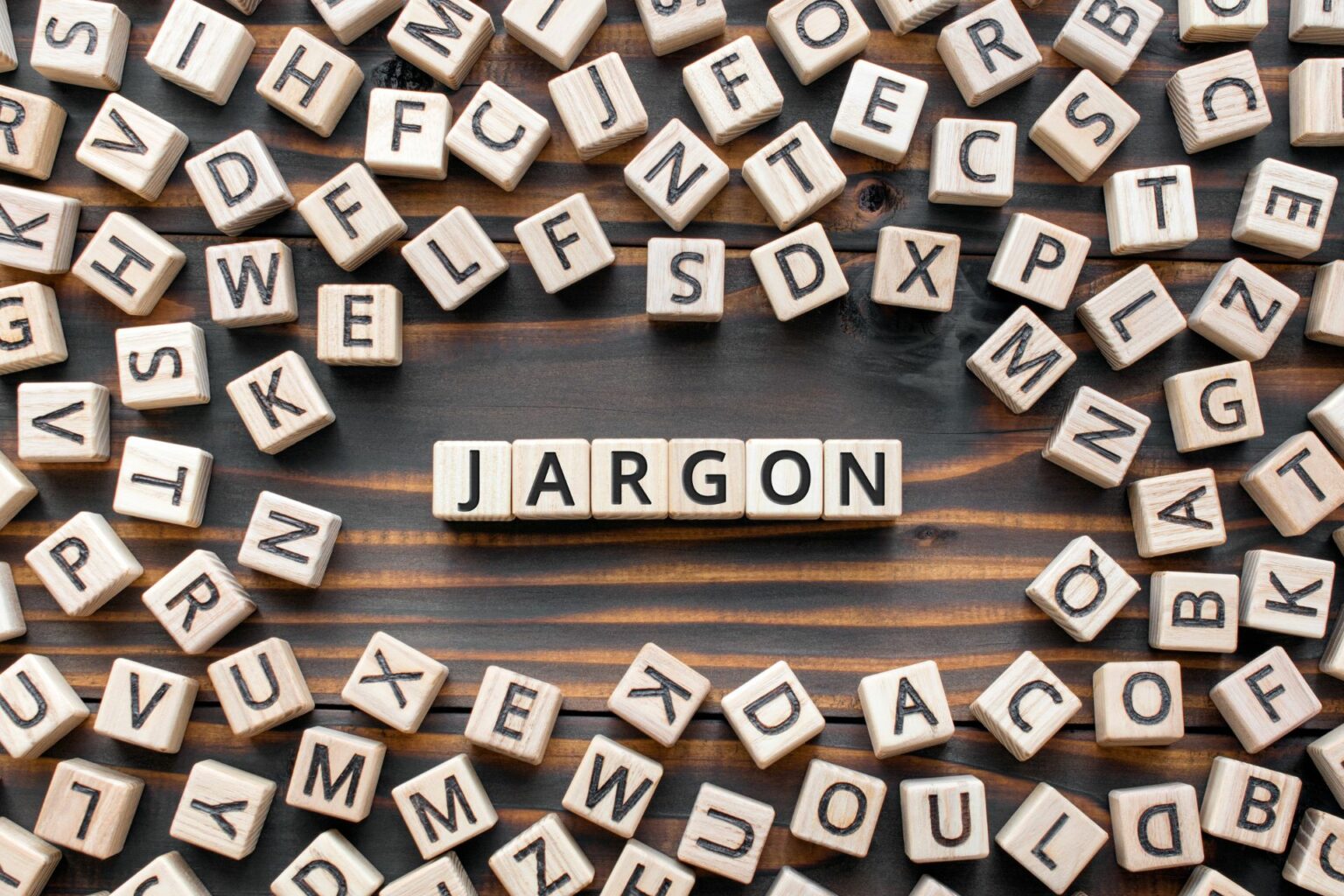 a table full randomly placed of Scrabble letters with the word JARGON spelt in the middle of the table