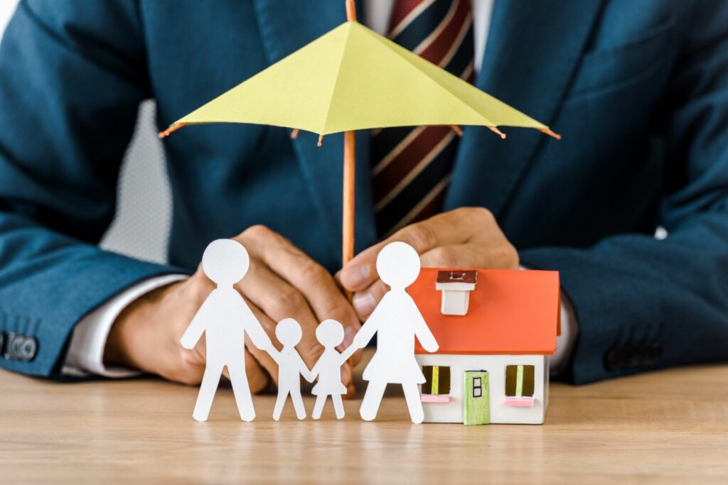 a umbrella protecting a paper cut out family and model home
